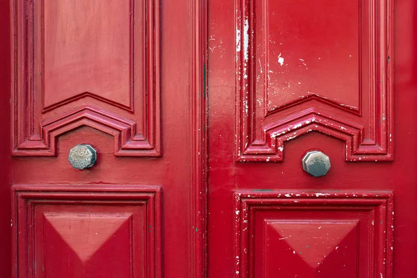 Bright red painted wooden door with geometric frames and peeling paint. Symmetric double door decorations and two old metal doorknobs. Architectural background. Vintage textures