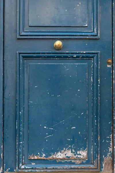 Shabby surface of framed door panel with round shiny brass doorknob. Scratched blue painted wooden door of old building in Paris France. Architecture details. Grunge textures