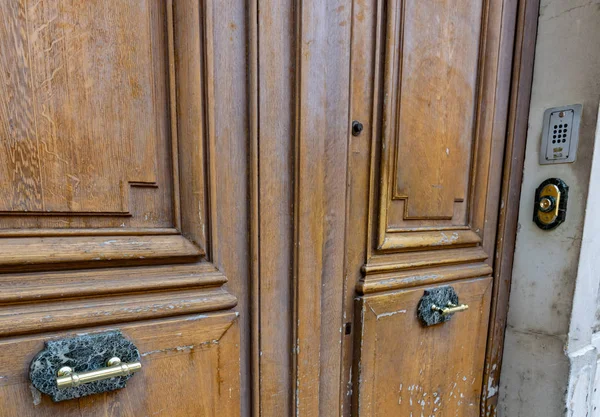 Brown wood double door panels with antique brass handles on black marble plates. Stone wall with code lock and intercom door bell near old wooden door. Grunge textures of architecture in Europe