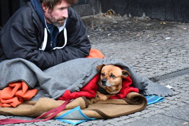 Berlin / Almanya - 12 09 2019: Evsiz fakir adam battaniyeye sarılmış köpekle yerde oturuyor.