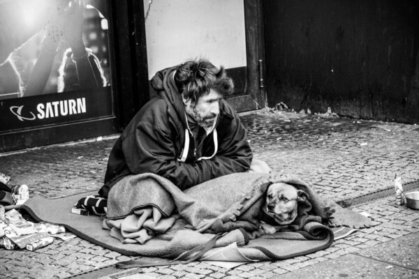Berlin / Germany - 12 09 2019: Homeless poor man sitting on ground with dog covered in blanket, Berlin, Germany Europe. 