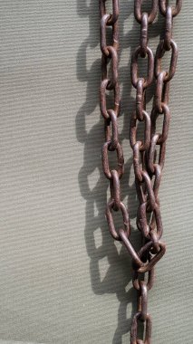 Koyu yeşil gölgeli, parlak güneş ışığı altında, kaba yeşil gri branda zemininde paslı metal zincirlere yakın çekim. Kırık demir zincirler özgürlük sembolü olarak