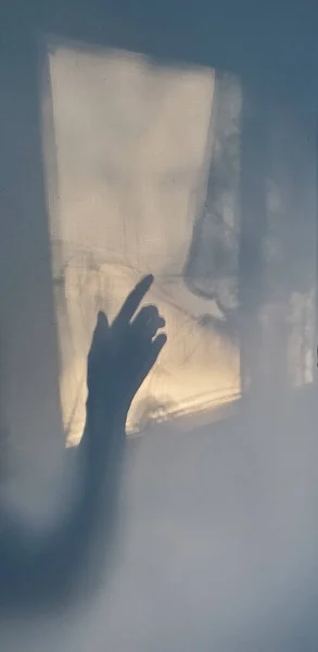 Creepy female hand shadow on wall. Defocus weird silhouette of hand touching lace curtain shadow