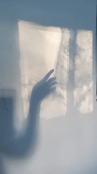 Blurry shadow of creepy hand silhouette looks like ghost out the window. Defocus palm of hand shadows on rough wall surface