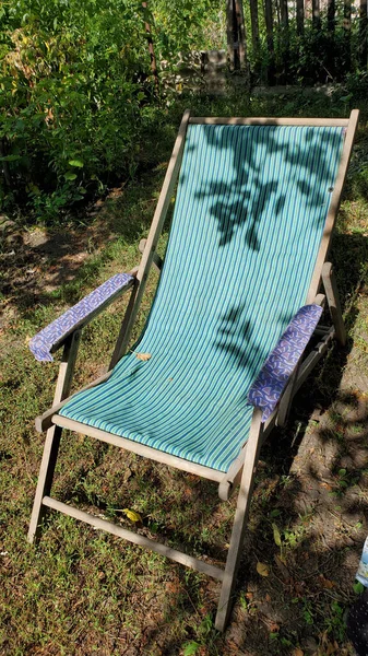 Retro deck chair with striped fabric hammock and shadows of tree branches with leaves. Outdoor furniture for backyard