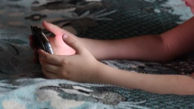 Küçük kız akşam evde akıllı telefon ekranında bir şeyler izliyor.