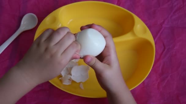 Çocuk parmaklarının pembe arka planda kaynamış yumurtayı kopyalama alanı ile soyduğu görünümün tam üstünde — Stok video