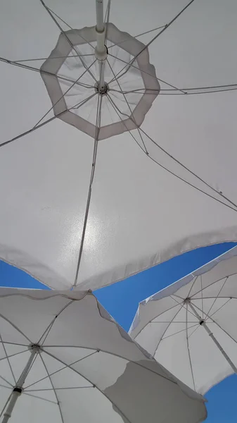 Travel themed abstraction of white sunshades on clear blue sky background with copy space. Sun shine through textile textures of beach umbrellas. Shot under sun parasols