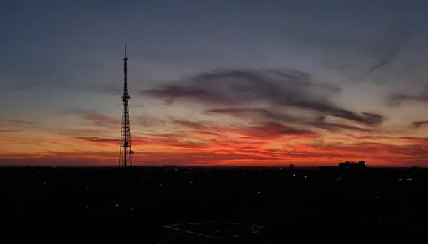 コミュニケーションタワーのシルエットで都会のスカイラインの上に息をのむような夕日の風景 暗い夜空の背景に紫と赤の雲 — ストック写真