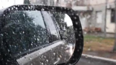 Yağmur damlalarıyla bulanık ayna görüntüsü. Yağmurlu bir hava. Damlayan yağmur damlalarından yansıyan bulanık yansımalı arabanın defocus dikiz aynası. Kötü yoldan geçerken yağmur yağar, tümsekler ve çukurlarla. Yağmurlu bir havada ıslak araba penceresinden dışarı bakıyorum.