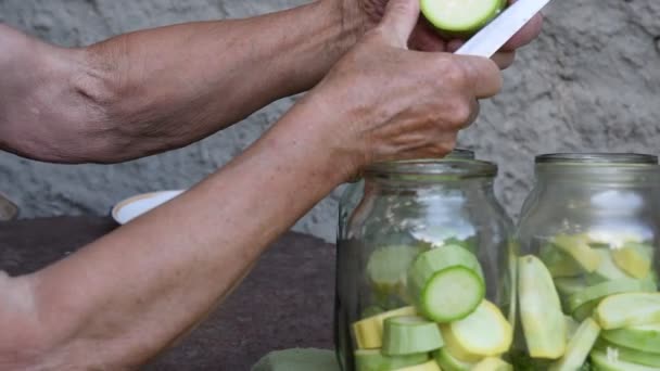 Stará žena ruce řezané čerstvé cukety na plátky a dát dovnitř skleněné sklenice pro domácí konzervování — Stock video