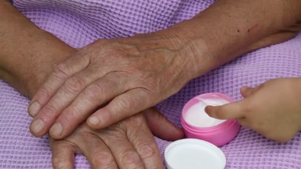 Kid finger take white cream and put to wrinkled skin of granny hand — Stock Video