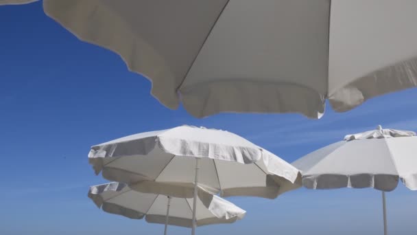 Sombrillas blancas contra el cielo azul claro. Símbolo de vacaciones de viaje — Vídeos de Stock