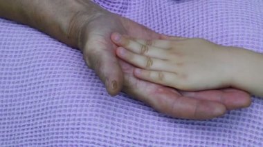 Kırışık avuç içi ve çocuğun eli birbirine dokunuyor. Torun ve büyükannenin yakın çekim elleri.