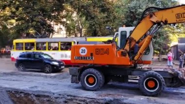Odessa / Ukrayna - 09 22 2020: Şehir caddesi inşaat halinde. Ağır makineli kazıcı ve şehir trafiği yoğun tozların arasında hareket ediyor. Kamera sola hareket ediyor. İnşaat işleri ve şehir trafiği