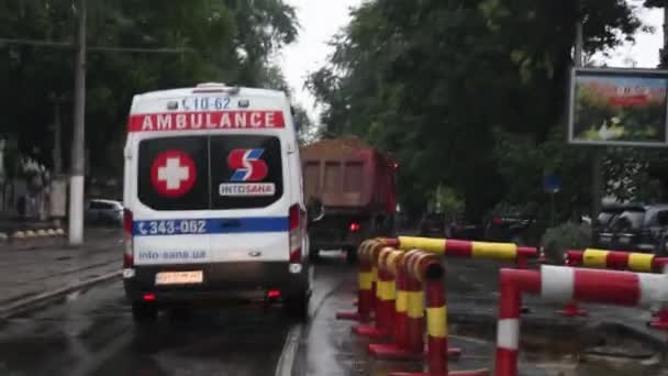 Vista instabile attraverso parabrezza bagnato durante lo spostamento dopo auto ambulanza e passare dalla ricostruzione stradale della città — Video Stock