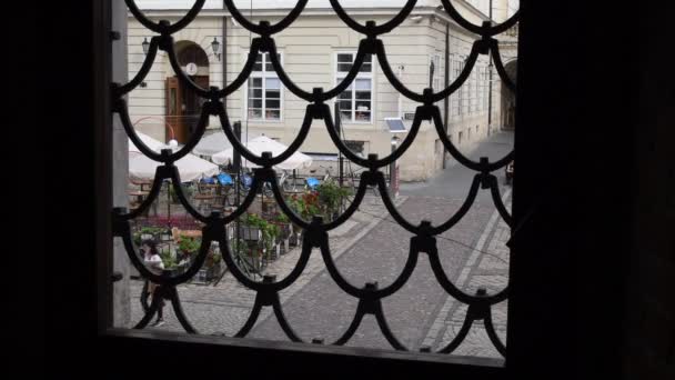 Los turistas caminan por el pavimento en la plaza Rynok en Lviv. Disparo a través de ventana de rejilla vintage — Vídeos de Stock