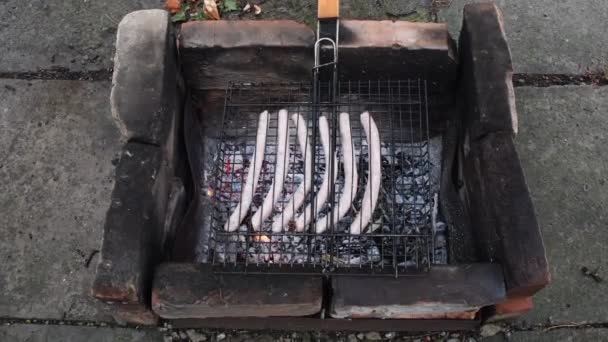 Grillen Bratwurst worsten voorbereiding op barbecue grill gemaakt van verbrande bakstenen — Stockvideo