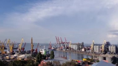 Limanda tahıl asansörü terminali ve konteynır alanı var. Yüksek gökyüzünde rüzgarlı bulutların altında sağa doğru endüstriyel deniz manzarası. Avrupa Karadeniz kıyısının limanındaki deniz manzarası. Kargo vinçleri ve tahıl asansörleriyle manzara. 4K kaydırma