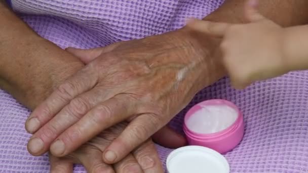 托德勒在手指上涂上白色润肤霜 并涂在老奶奶的皮肤手上 80岁的祖母和4岁的孙子孙女的不同的手 老年皮肤护理的概念 小孩子用手指涂白霜 涂在老太太的皱纹皮肤上 — 图库视频影像