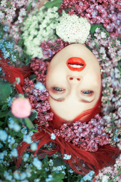 beautiful young woman with red hair lying in colorful flowers, close up face with perfect make up