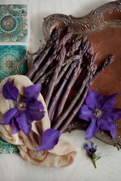 新鲜的深绿色 紫罗兰色芦笋装饰在老式的板材与美丽的紫罗兰铁线莲花和绿松石东方图案 可用作背景 — 图库照片