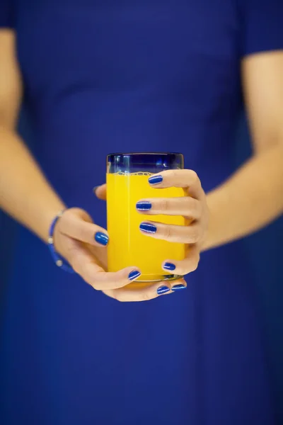 Beautiful woman hands holding glass of bright yellow orange soda in front of her blue dress, can be used as background