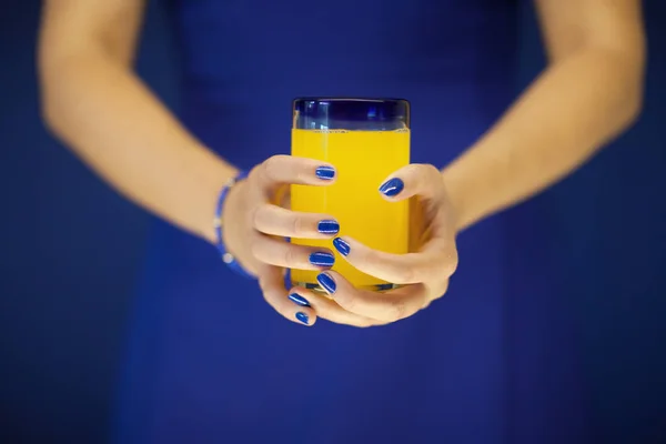 Beautiful woman hands holding glass of bright yellow orange soda in front of her blue dress, can be used as background