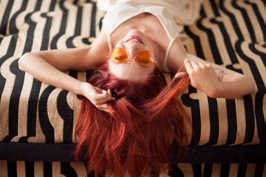 Genç ve güzel kadın Kızıl saçlı ve güneş gözlüğü rahat yatıyor ve kanepede gülüyor, duygu kavramı ateş