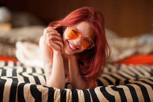 漂亮的年轻女子 红色的头发和太阳镜躺在沙发上放松和笑 情绪概念拍摄 — 图库照片