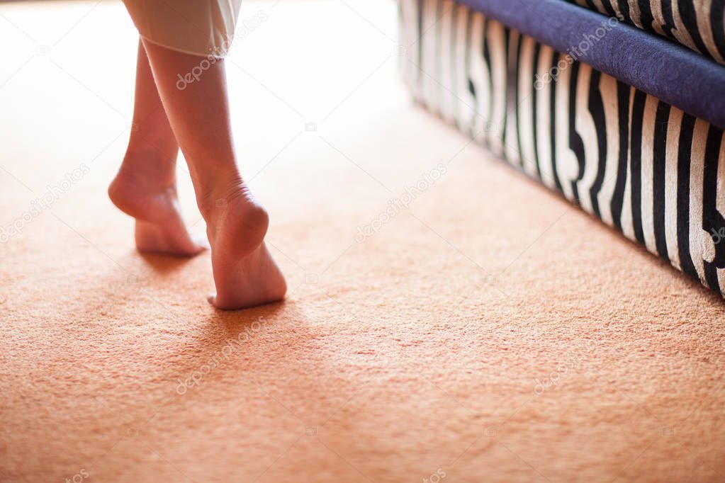 young woman's feet close up, walking on tiptoe on a soft carpet floor, into window light