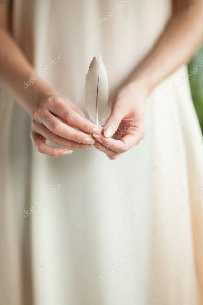 woman hand holding bird feather, sensual studio shot with soft light background