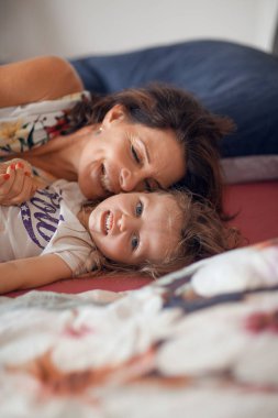 güzel anne kıkırdayarak ve gülüyor ve öpüşme, güzel bir mutlu aile sahne kızıyla yatakta, kucaklamaları 