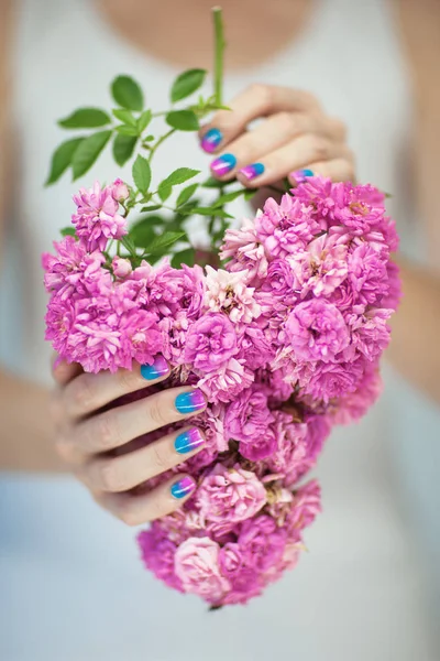 Beautiful woman hands with perfect violet pink and turquoise nail polish holding pink roses, can be used as background