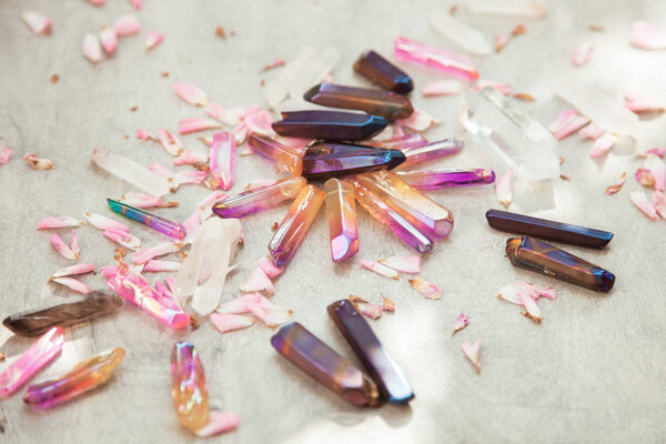 Colorful quartz crystals with pink rose leaves on wooden structure, flat lay background 