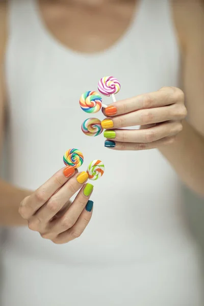 Beautiful woman hands with rainbow nail polish holding colorful swirl lollypops, funny cheerful, can be used as background