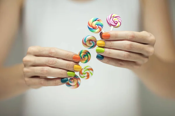 美丽的女人手用彩虹指甲油捧着五颜六色的漩涡 Lollypops 滑稽开朗 可作背景 — 图库照片