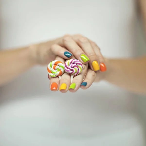 美丽的女人手用彩虹指甲油捧着五颜六色的漩涡 Lollypops 滑稽开朗 可作背景 — 图库照片