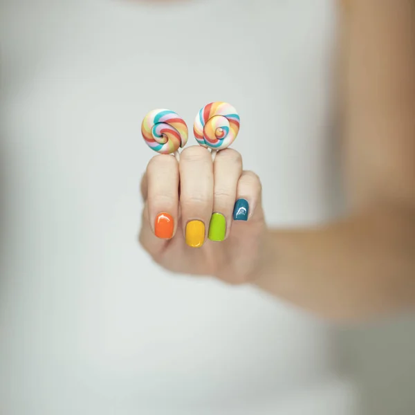 Beautiful woman hands with rainbow nail polish holding colorful swirl lollypops, funny cheerful, can be used as background