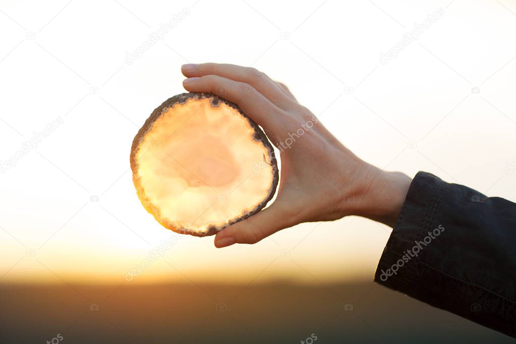 Beautiful woman hands holding agate slice crystal in the sunlight, healing crystal concept shoot, can be used as background 