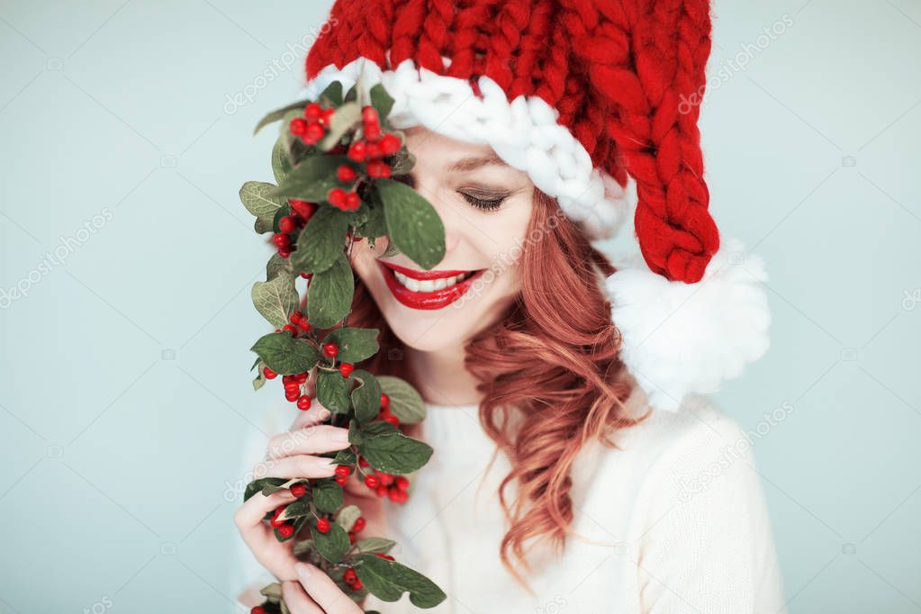 Santas little helper. Beautiful happy young woman with a santa claus hat, perfect make up, red lipstick, holding branch with red berries