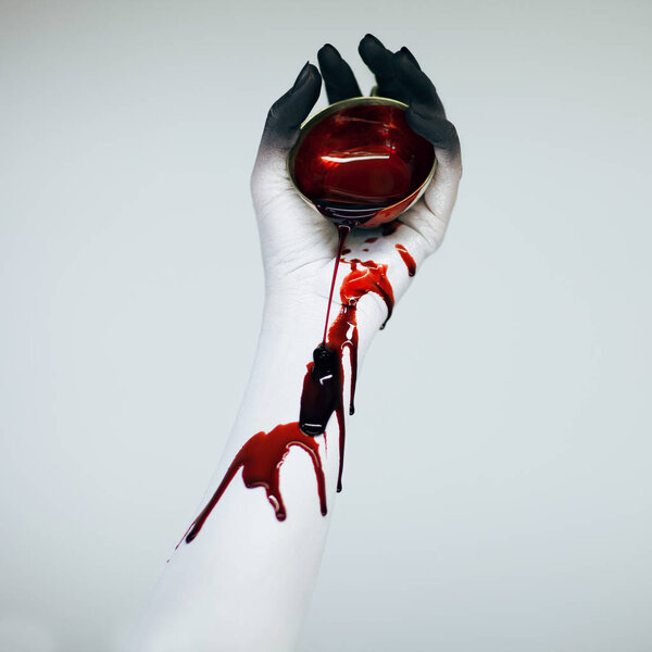 Creepy Halloween bloody woman monster hand and arm with white and black make up holding vintage cup with blood in front of white background