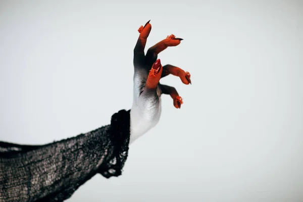 Creepy Halloween monster witch hand with white, red and black make up and long creepy fingernails in front of white background