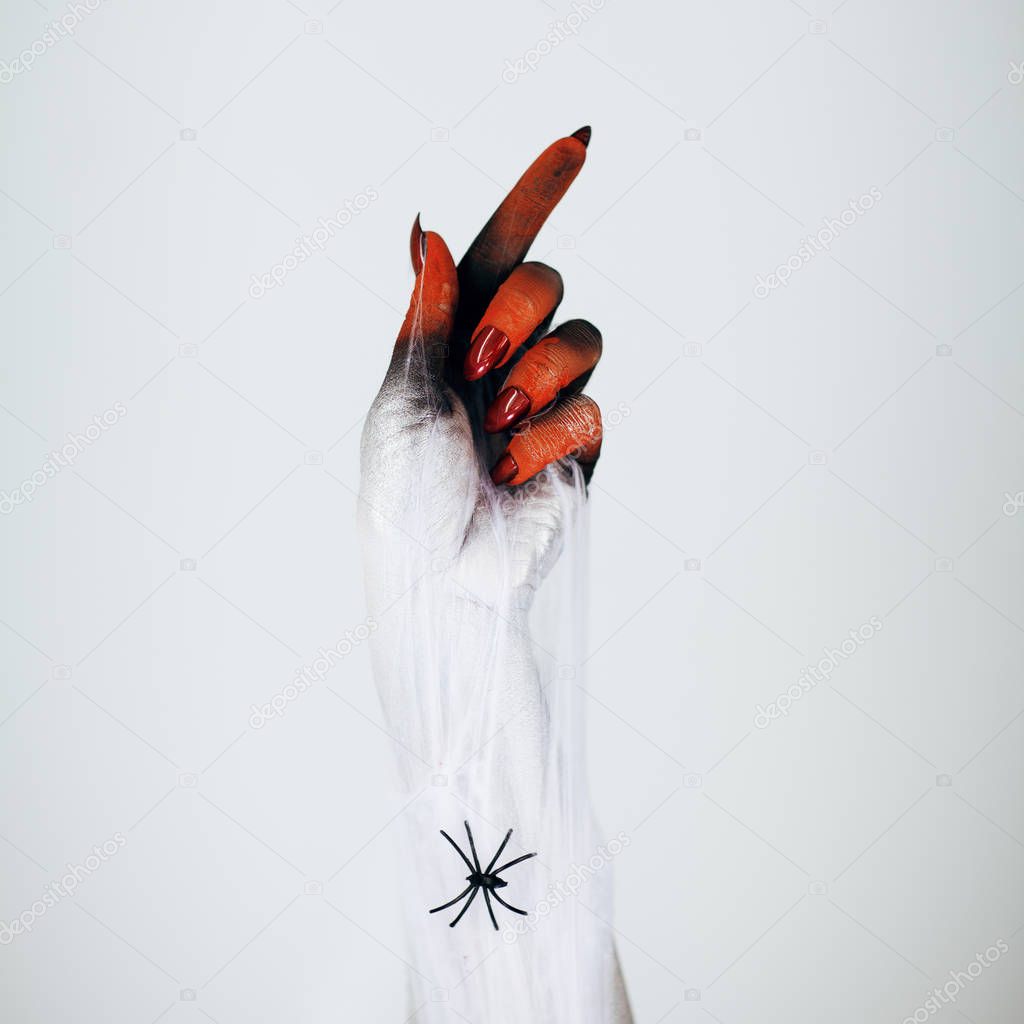 Creepy Halloween monster witch hand with white, red and black make up and long creepy fingernails and spiderweb in front of white background