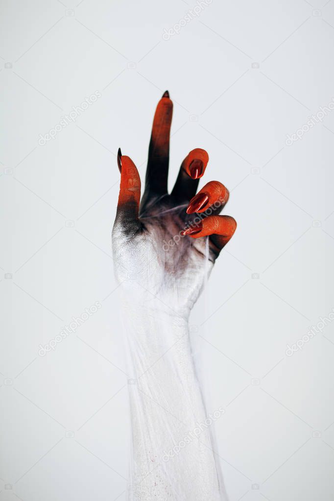 Creepy Halloween monster witch hand with white, red and black make up and long creepy fingernails and spiderweb in front of white background
