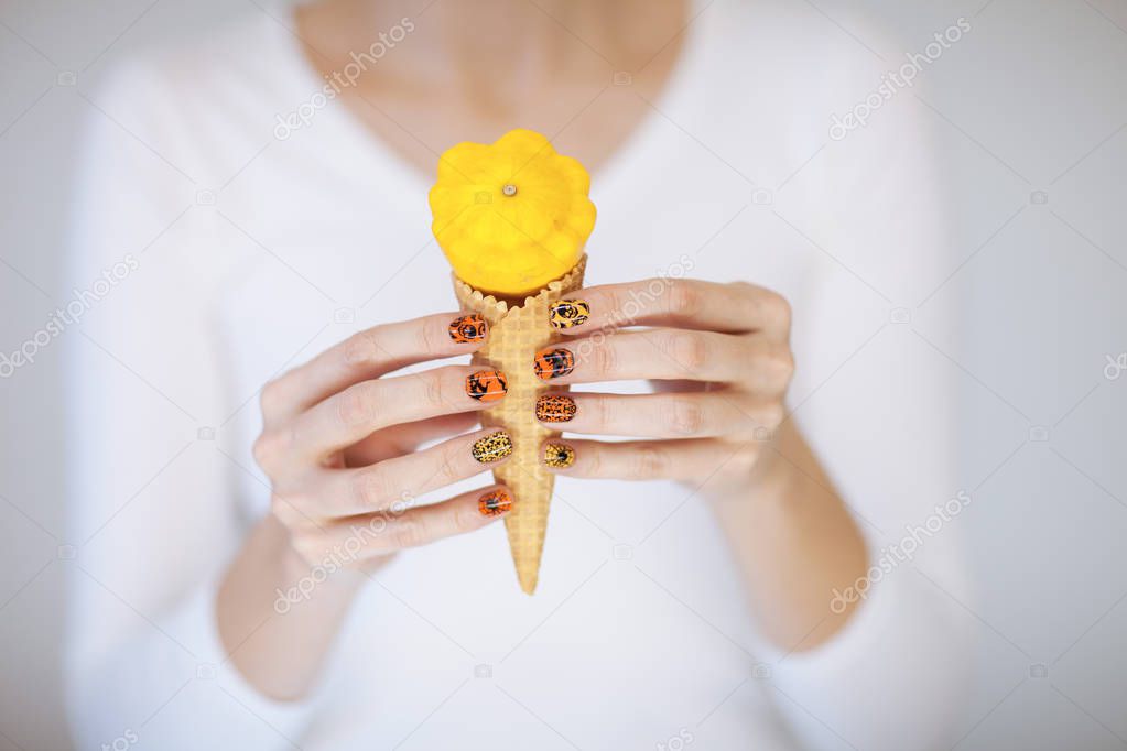 Beautiful woman hands with cute halloween nail polish holding ice cream cone with little pumpkin can be used as background