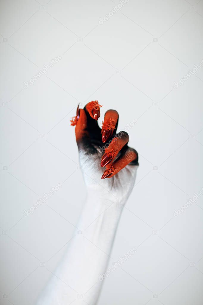 Creepy Halloween monster witch hand with white, red and black make up and long creepy fingernails in front of white background