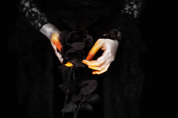 Creepy halloween vampire hands close up in red orange and silver holding black rose, can be used as background