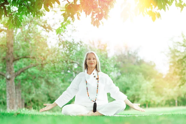 Güzel, en iyi yaş, uzun gri saçlı, dışarıda yoga egzersizi yapan son sınıf öğrencisi kadın.