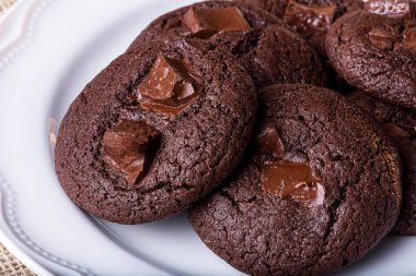 Beyaz tabakta ev yapımı çikolatalı kurabiyeler. Tahta bir masada.